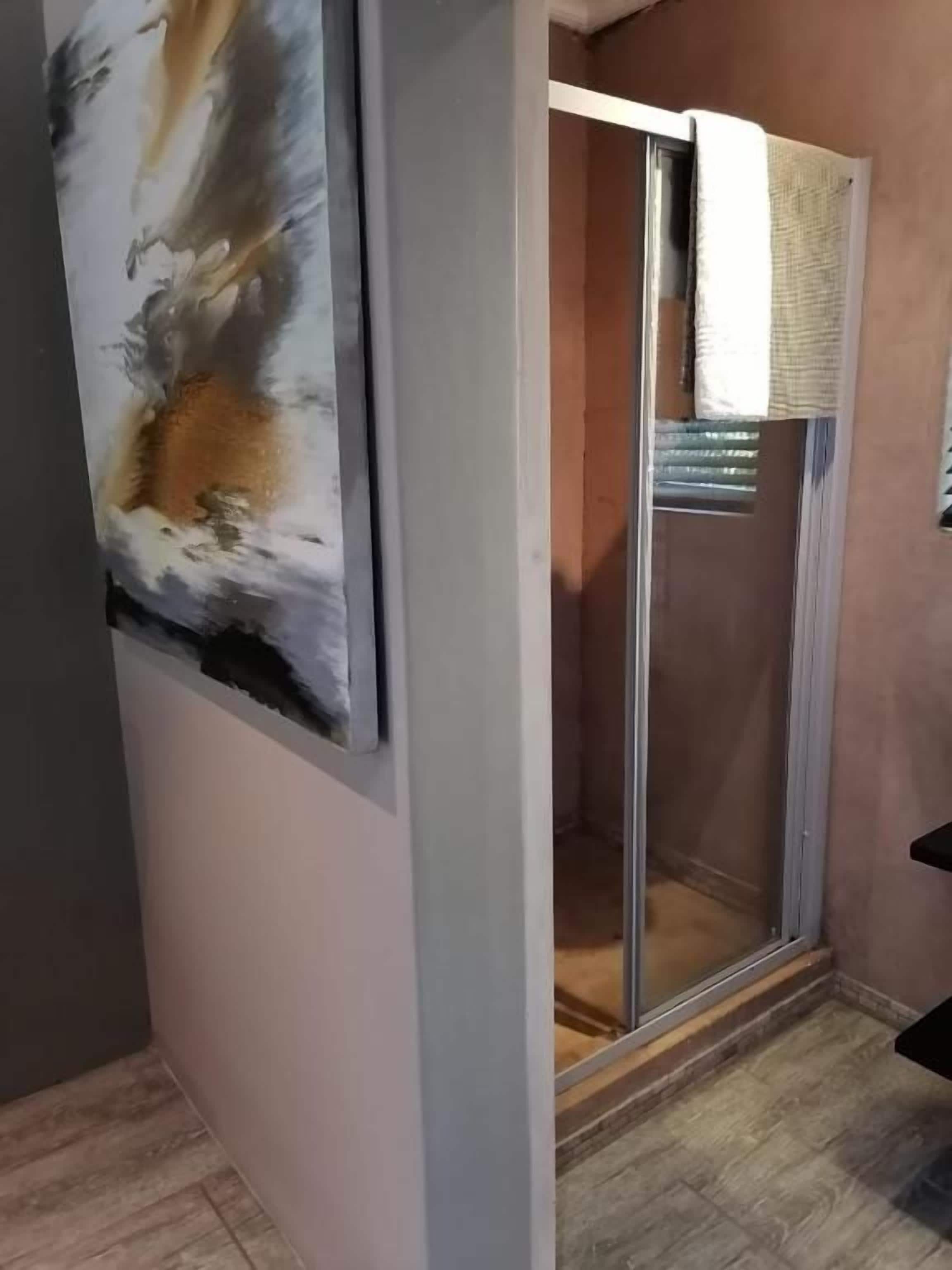 A room with a sliding glass door leading to a shower area, a painting on the wall, and a towel hanging on the door.