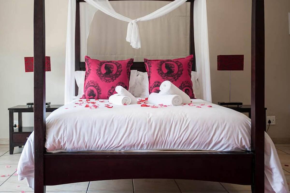 Un lit à baldaquin avec une literie blanche et des oreillers roses, un tapis rouge et un ciel de lit blanc.
