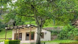 A small, single-story building with a covered porch, surrounded by lush greenery and a rocky hillside. - The duBoirs Boutique Lodge (Waterfall)