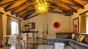 A spacious living room with a high wooden ceiling, a modern chandelier, a grey sofa, and a dining area with clear chairs. - The duBoirs Boutique Lodge (Waterfall)