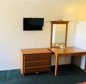 A room with a wooden desk, a mirror, a television mounted on the wall, and a telephone on the desk.