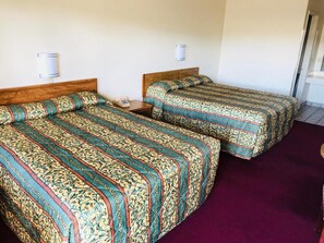 Two single beds with patterned bedding, a bedside table with a lamp, and a bathroom door in the background. - Sands Motel (Ontario)