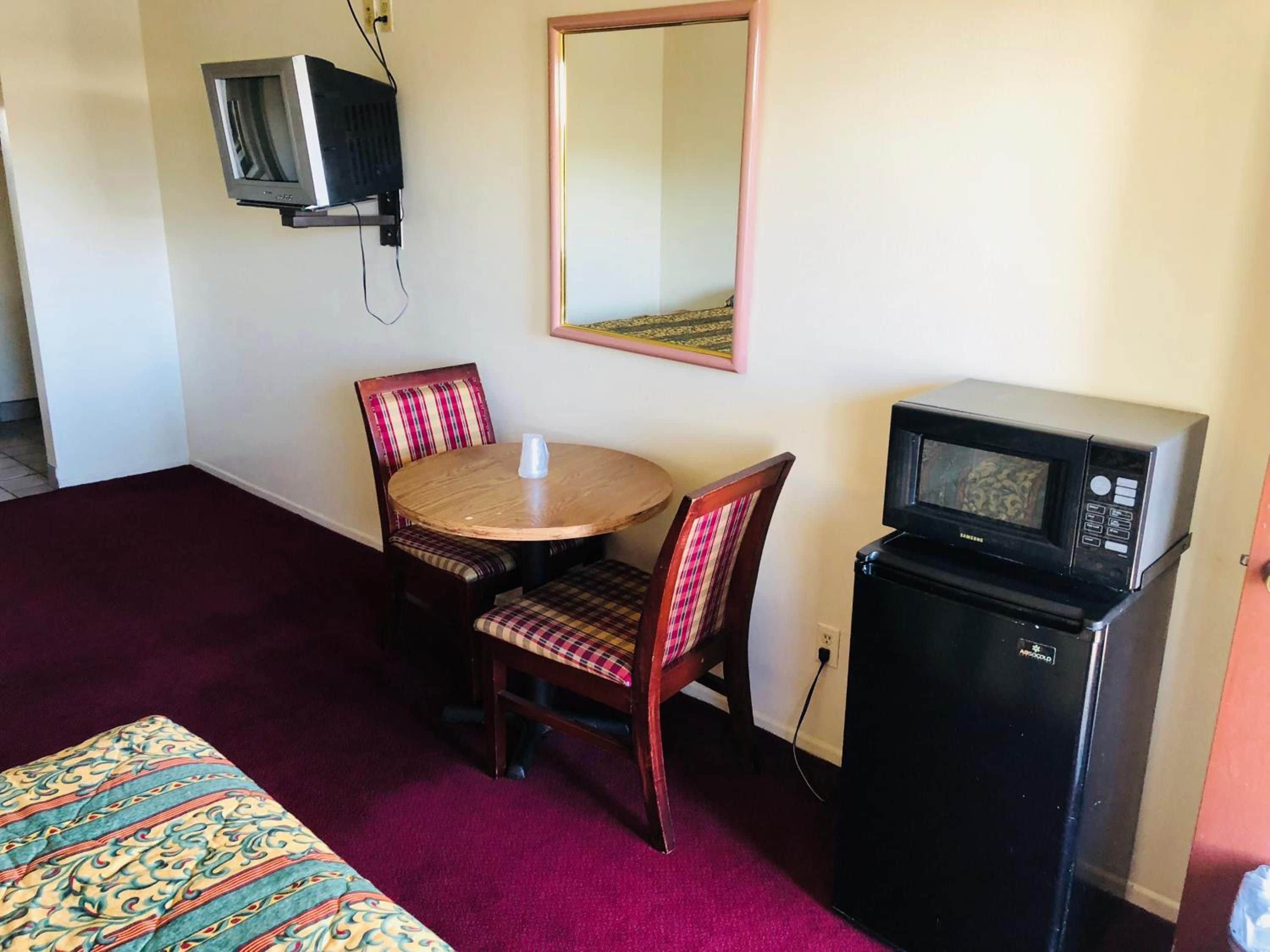 A small room with a bed, a table with chairs, a microwave, and a television.