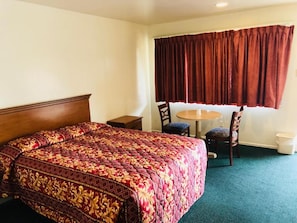 A hotel room with a large bed, a round table, two chairs, a small bedside table, and a window with curtains.