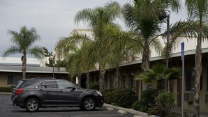 A parking lot with a dark-colored SUV parked near a building with palm trees. - Sands Motel (Ontario)