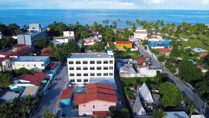 An aerial view of a coastal town with a prominent white building, narrow streets, and palm trees. - Pousada Sal e Mar (Ipojuca)