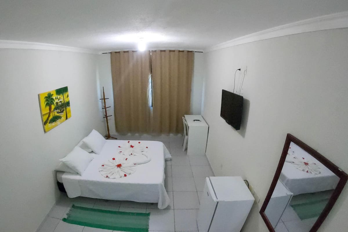 A hotel room with a bed, a small table, a television, and a mirror.