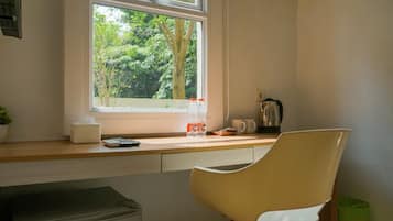 Une cuisine avec une fenêtre, une chaise, une poubelle et une machine à café.