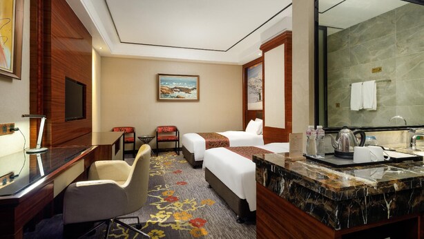 Une chambre d’hôtel équipée d’un bureau, de deux lits, d’une chaise, d’un tableau, d’une salle de bain avec un miroir et d’un comptoir en marbre.