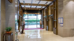 Un hall d’hôtel moderne avec un sol en marbre, un comptoir d’accueil et une porte vitrée donnant sur l’extérieur.