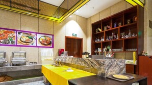 Un restaurant avec un comptoir en marbre, une table jaune et une étagère où sont posés des verres et des bouteilles.