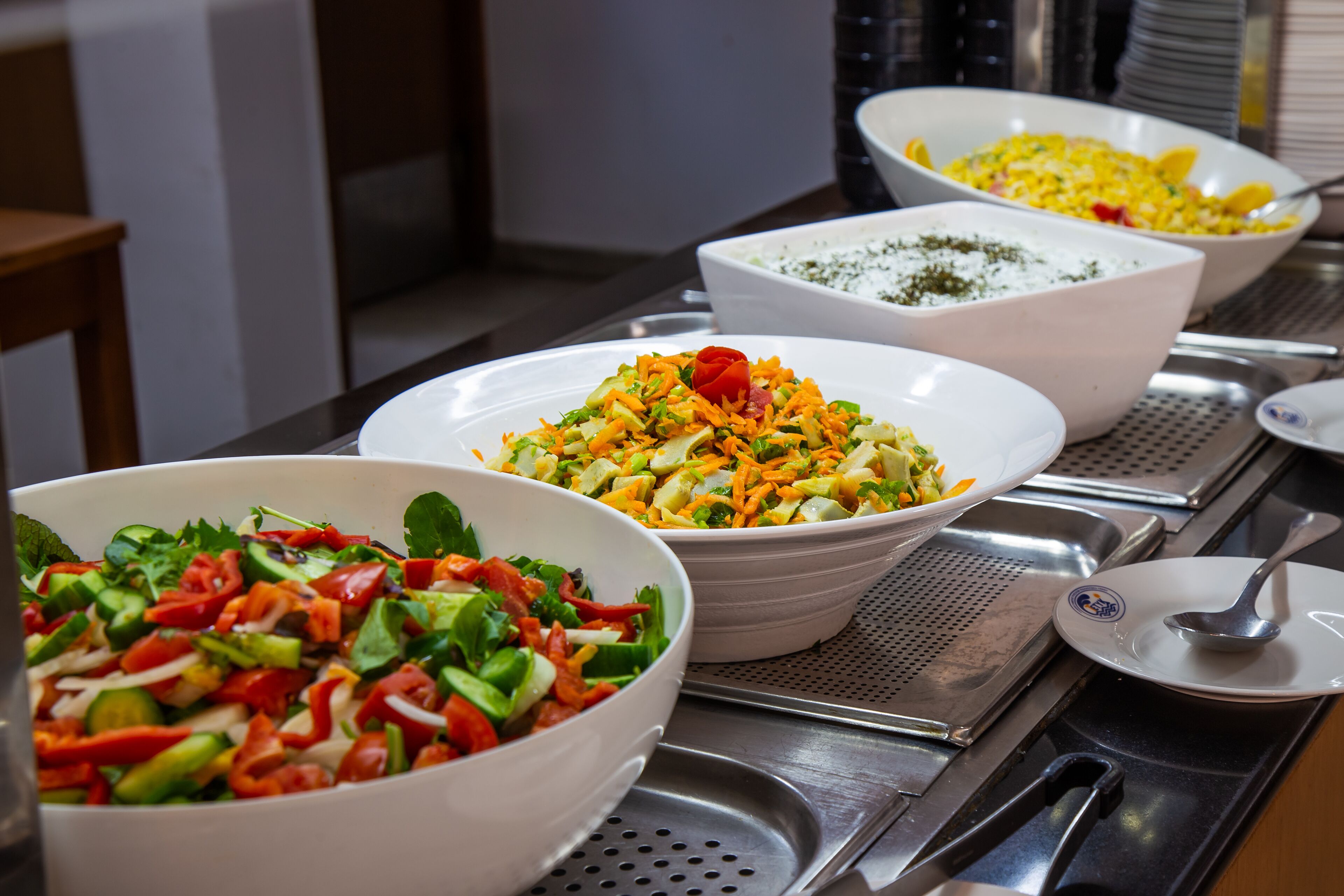 Une table de buffet proposant divers plats, notamment des salades et un saladier de maïs.