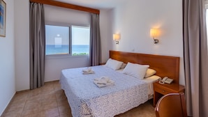 A hotel room with a large bed, two bedside lamps, a wooden headboard, a nightstand with a phone, and a view of the sea through a window. - Tetyk Hotel  (Paralimni)