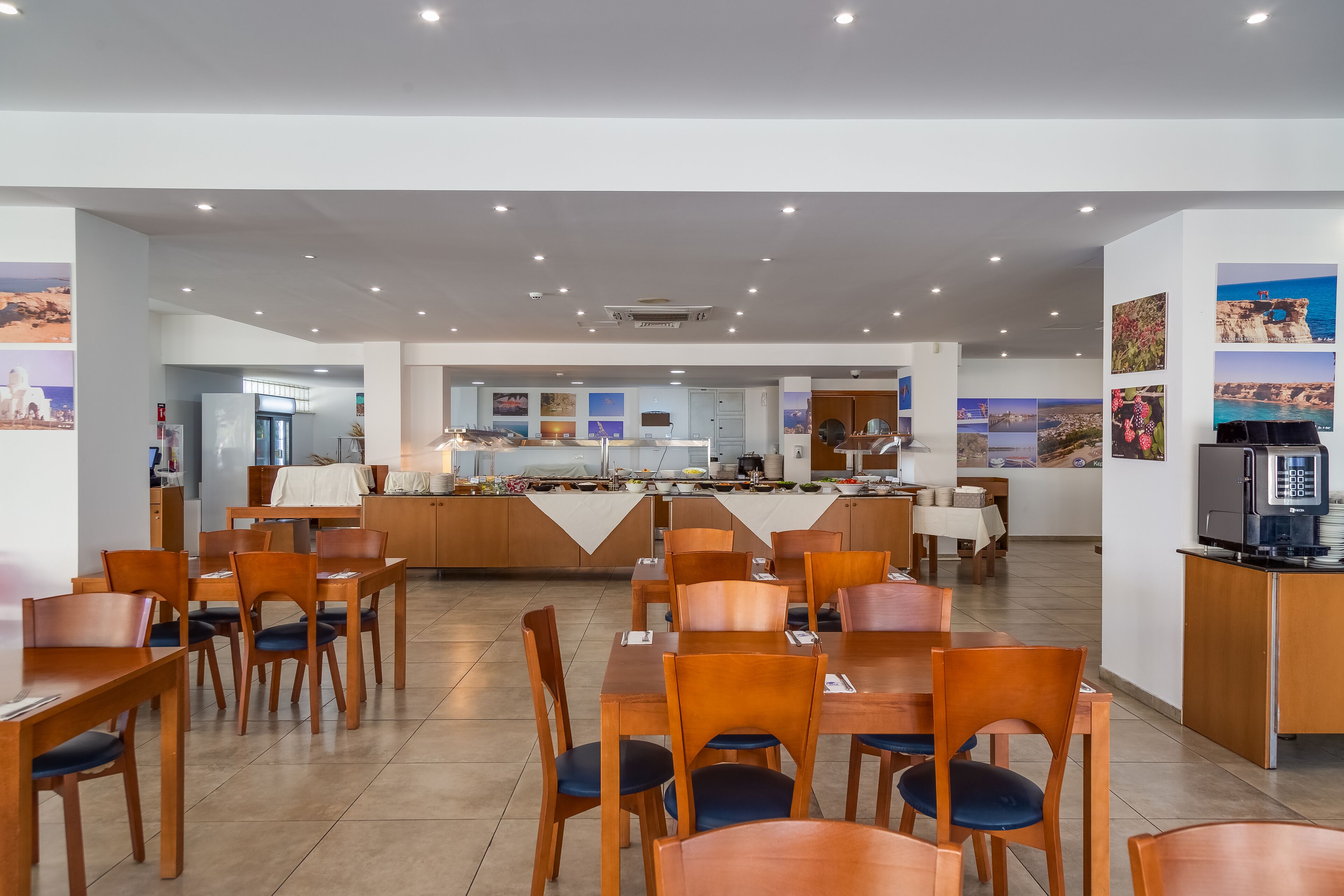 A spacious dining area with wooden tables and chairs, a central buffet, and a kitchen area.