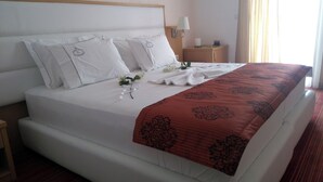 A hotel room with a large bed, white bedding, a red patterned throw, and a nightstand with a lamp. - Santa Quaranta Premium Resort (Sarandë)