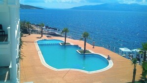 A pool with a unique shape, surrounded by palm trees and a view of the sea. - Santa Quaranta Premium Resort (Sarandë)