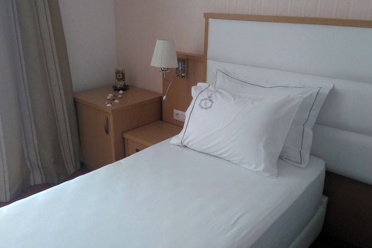 A hotel room with a bed, a nightstand, a lamp, and a wall-mounted light fixture.