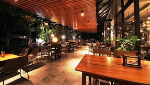 An indoor restaurant with wooden tables and chairs, ambient lighting, and potted plants. - Hay Bandung (Bandung)