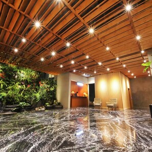 Una hall con soffitto in legno, reception, area salotto e una fontana.