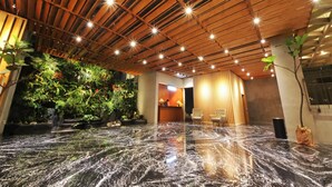 A lobby with a wooden ceiling, a reception desk, seating area, and a water feature. - Hay Bandung (Bandung)