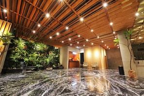 A lobby with a wooden ceiling, a reception desk, seating area, and a water feature. - Hay Bandung (Bandung)