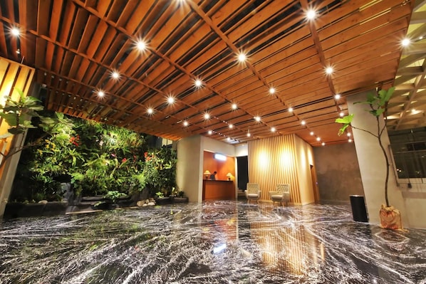 A lobby with a wooden ceiling, a reception desk, seating area, and a water feature. - Hay Bandung (Bandung)
