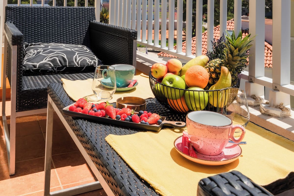 En balkon med fletningsmøbler, et bord med en skål frugt, en kop samt en bakke med jordbær og blåbær.