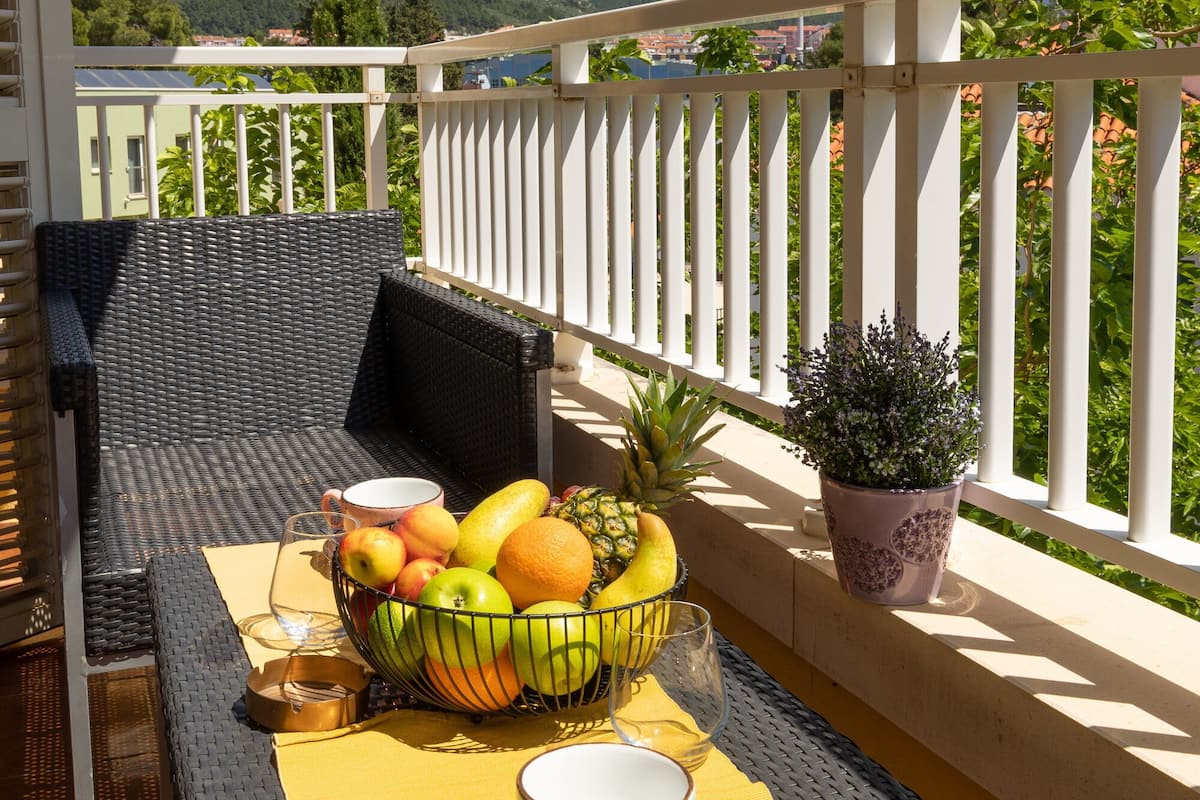 En balkon med fletmøbler, et bord med en skål med frugt, en potteplante og en storslået udsigt over bjergene.