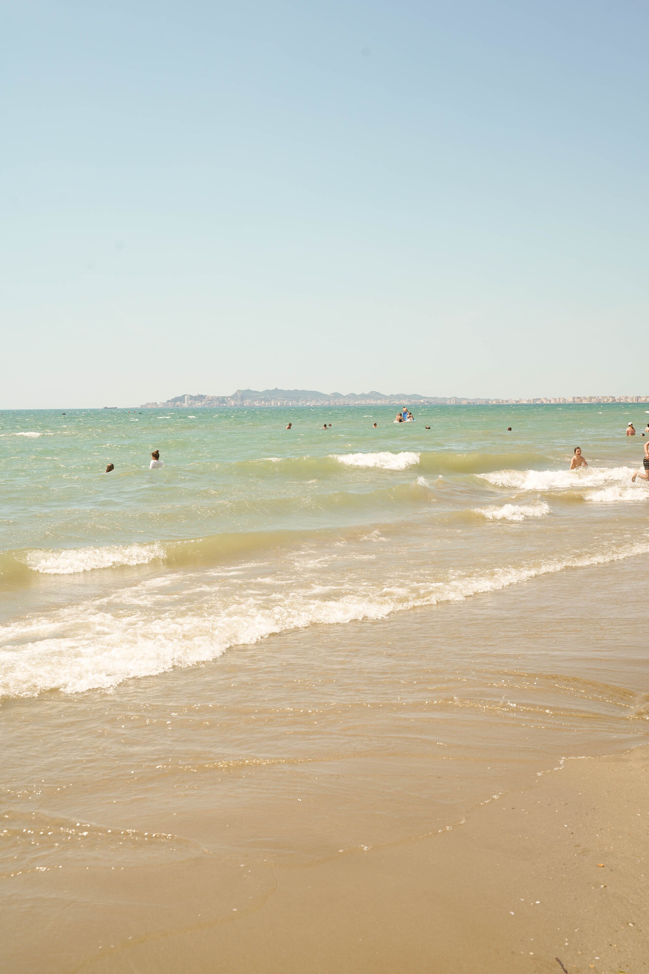 A beach with clear water and a distant city skyline.