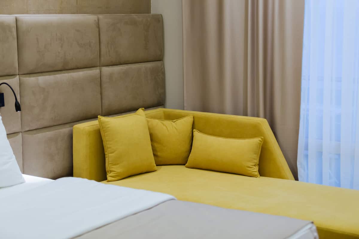 Una habitación de hotel con una cama, un sofá amarillo y un cabecero.