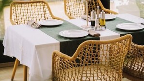 Un comedor con sillas de mimbre, una mesa dispuesta con platos, cubiertos y una vela.