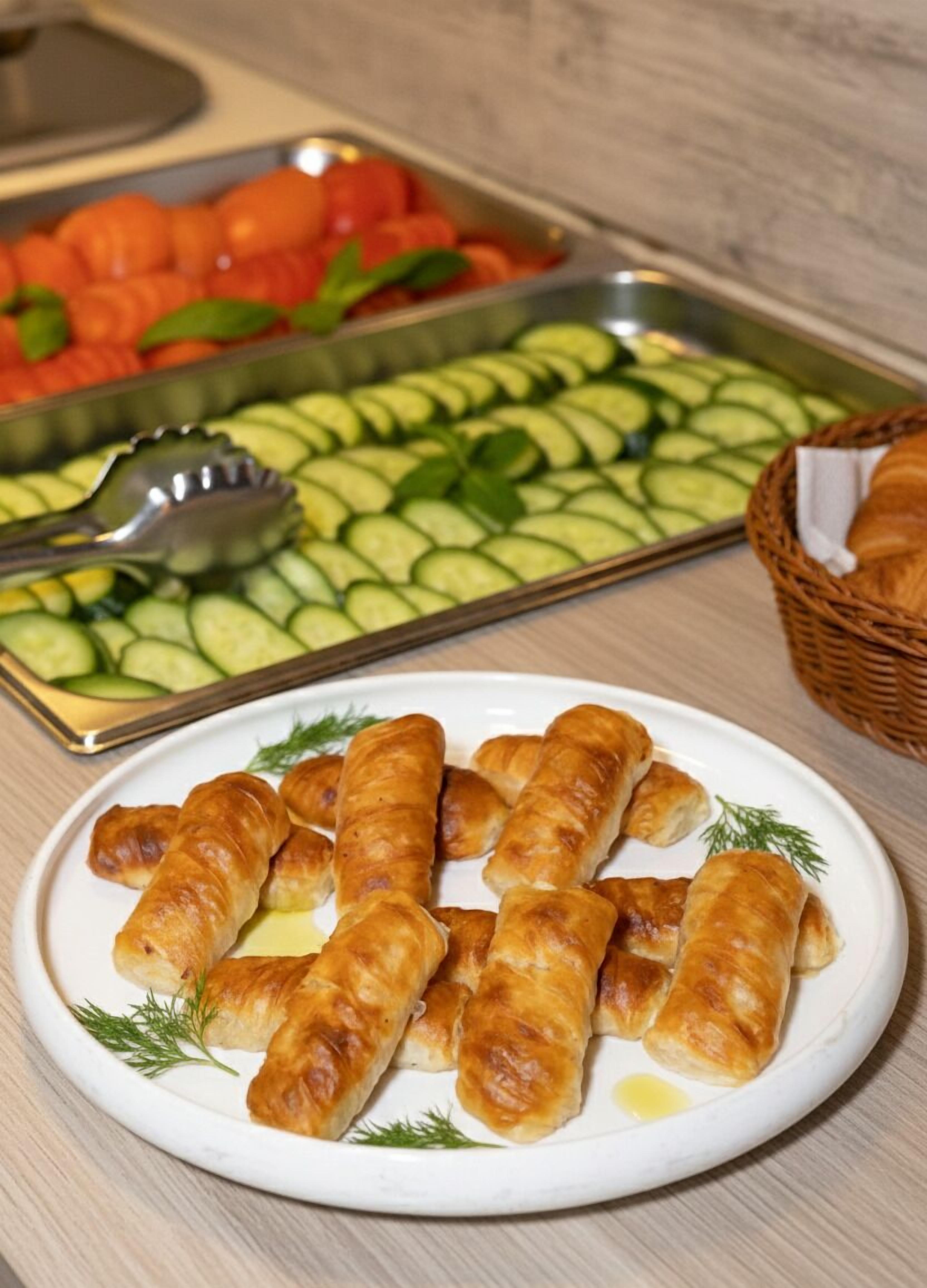 Un plato de pasteles dorados, una bandeja de pepinos en rodajas y una cesta de pan sobre una mesa.