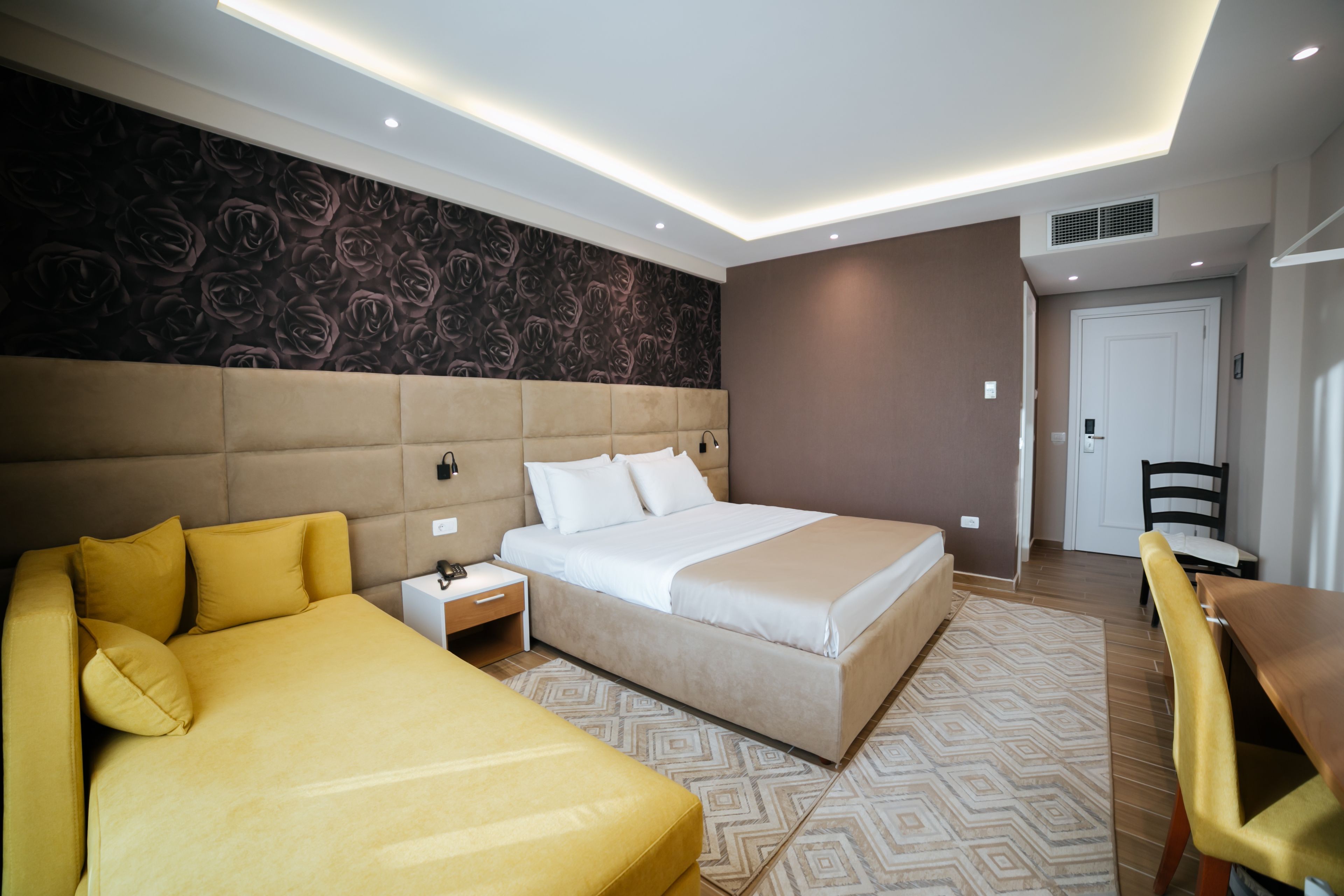 A modern hotel room with a large bed, a sofa, a desk, and a chair.