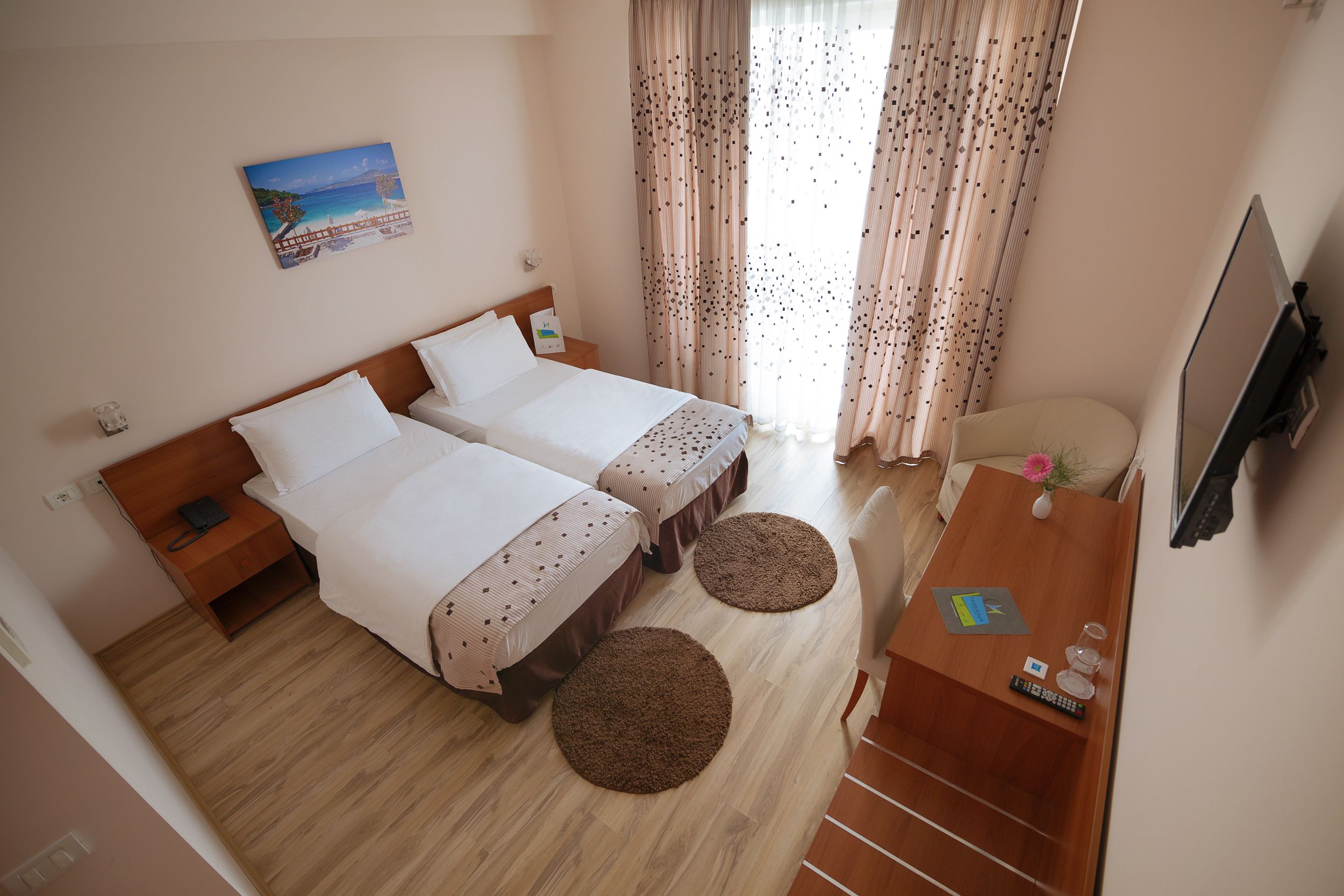 A hotel room with two beds, a wooden desk, a TV, and a painting on the wall.