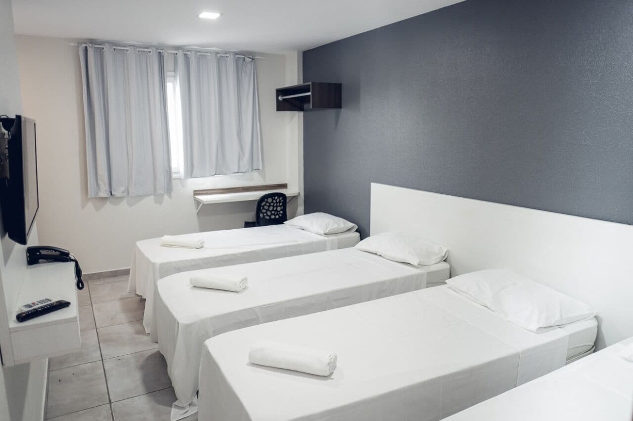 A hotel room with two single beds, a desk with a telephone, and a TV mounted on the wall.