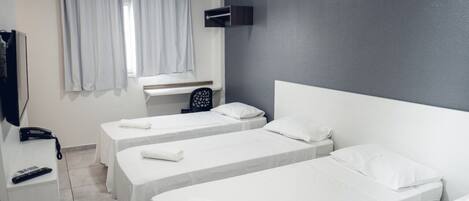 A hotel room with two single beds, a desk with a telephone, and a TV mounted on the wall.