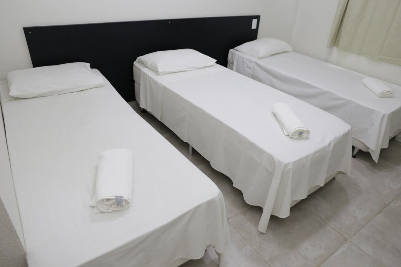 A room with three single beds, each with white linens and pillows, and a black headboard.