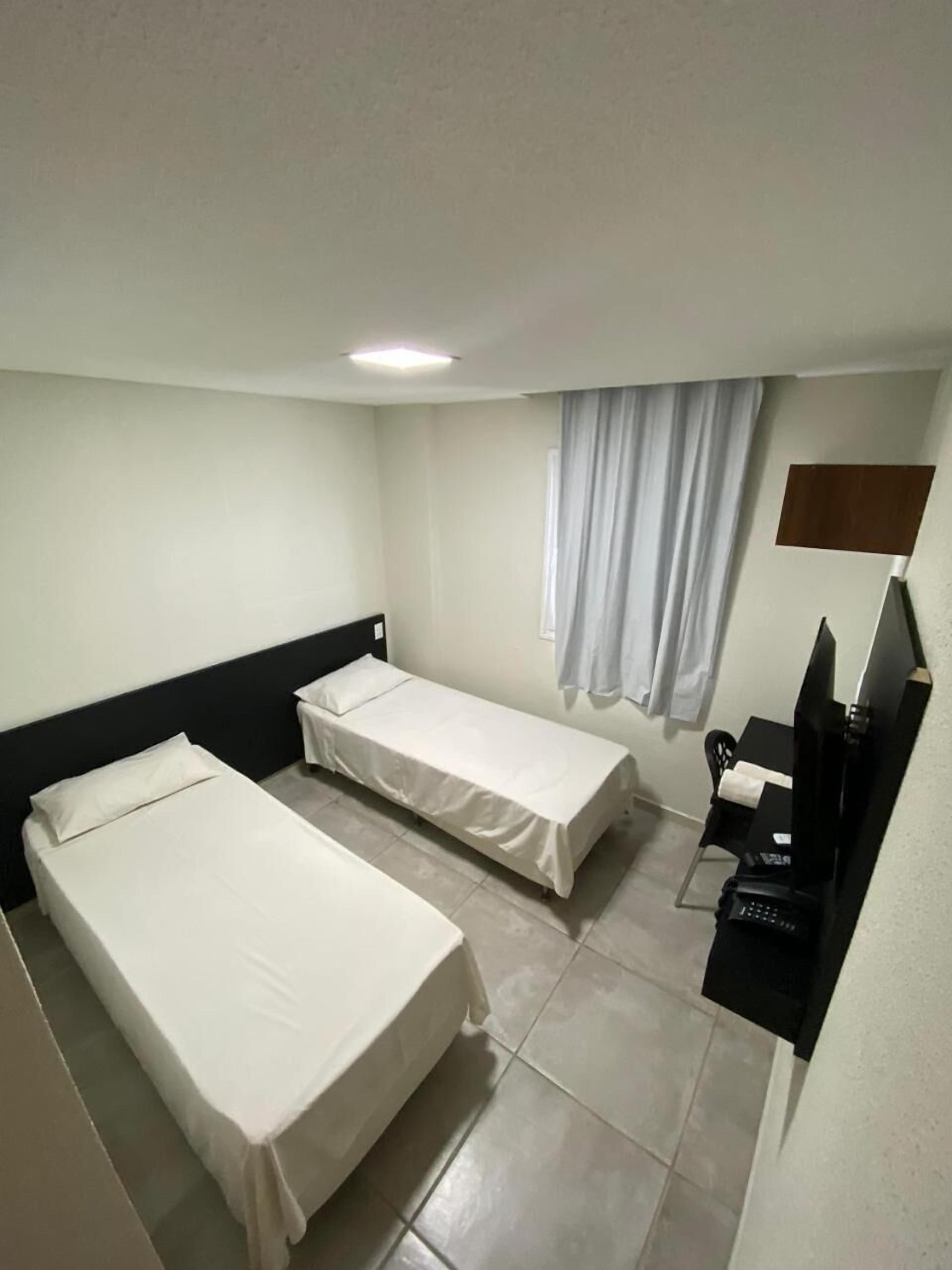 Una habitación de hotel con dos camas individuales, un escritorio con ordenador y una televisión.