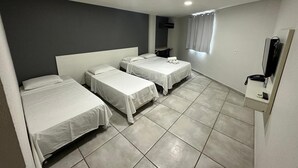 A hotel room with three single beds, a flat-screen TV, a telephone, and a small table.
