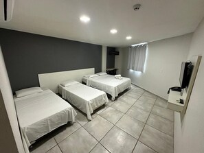 A hotel room with three single beds, a flat-screen TV, a telephone, and a small table.