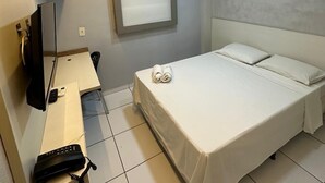 A hotel room with a bed, a desk with a telephone, a television, and a window with blinds.