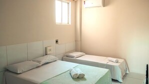 Une petite chambre propre, équipée de deux lits simples, d’une fenêtre, d’un climatiseur et d’une prise de courant au mur.