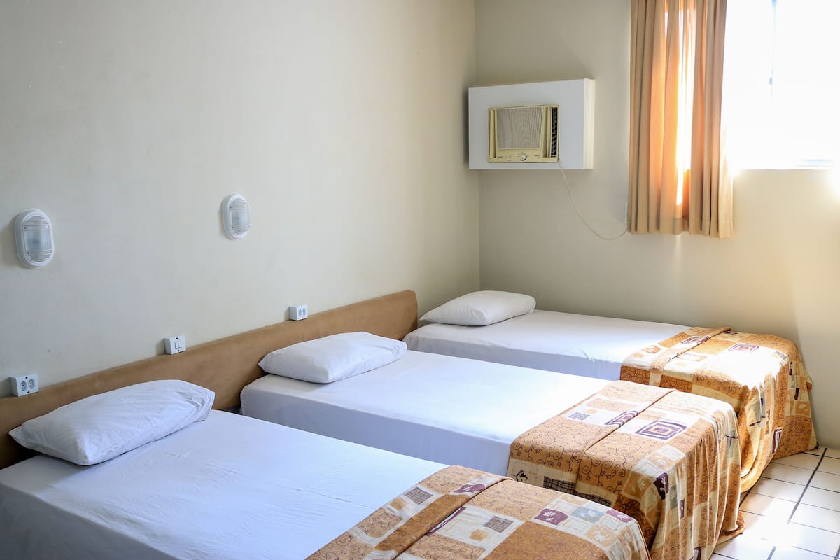 A room with three single beds, a wall-mounted air conditioner, and a window with curtains.