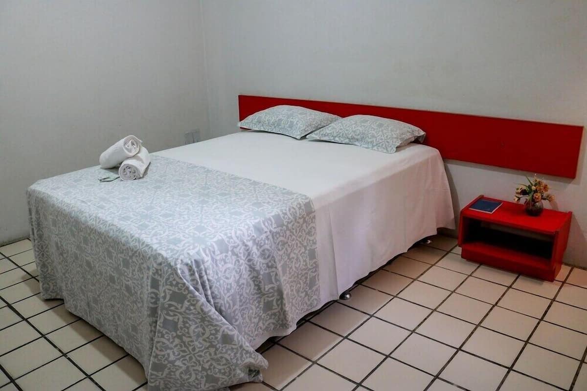 A hotel room with a bed, a red headboard, a bedside table with a red nightstand, and a white telephone.