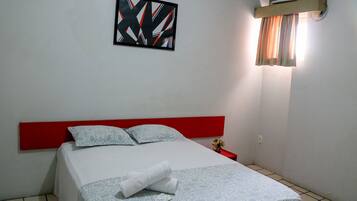 A neatly made bed with a red headboard, a framed abstract artwork on the wall, and a window with curtains.