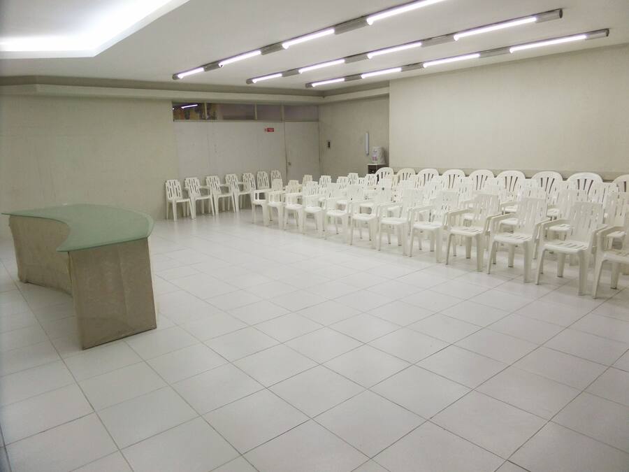 A conference room with a long row of white plastic chairs, a green table, and fluorescent ceiling lights.
