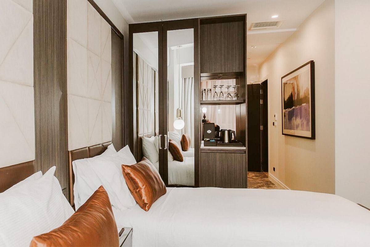 Una habitación de hotel con una cama grande, un minibar y un espejo.