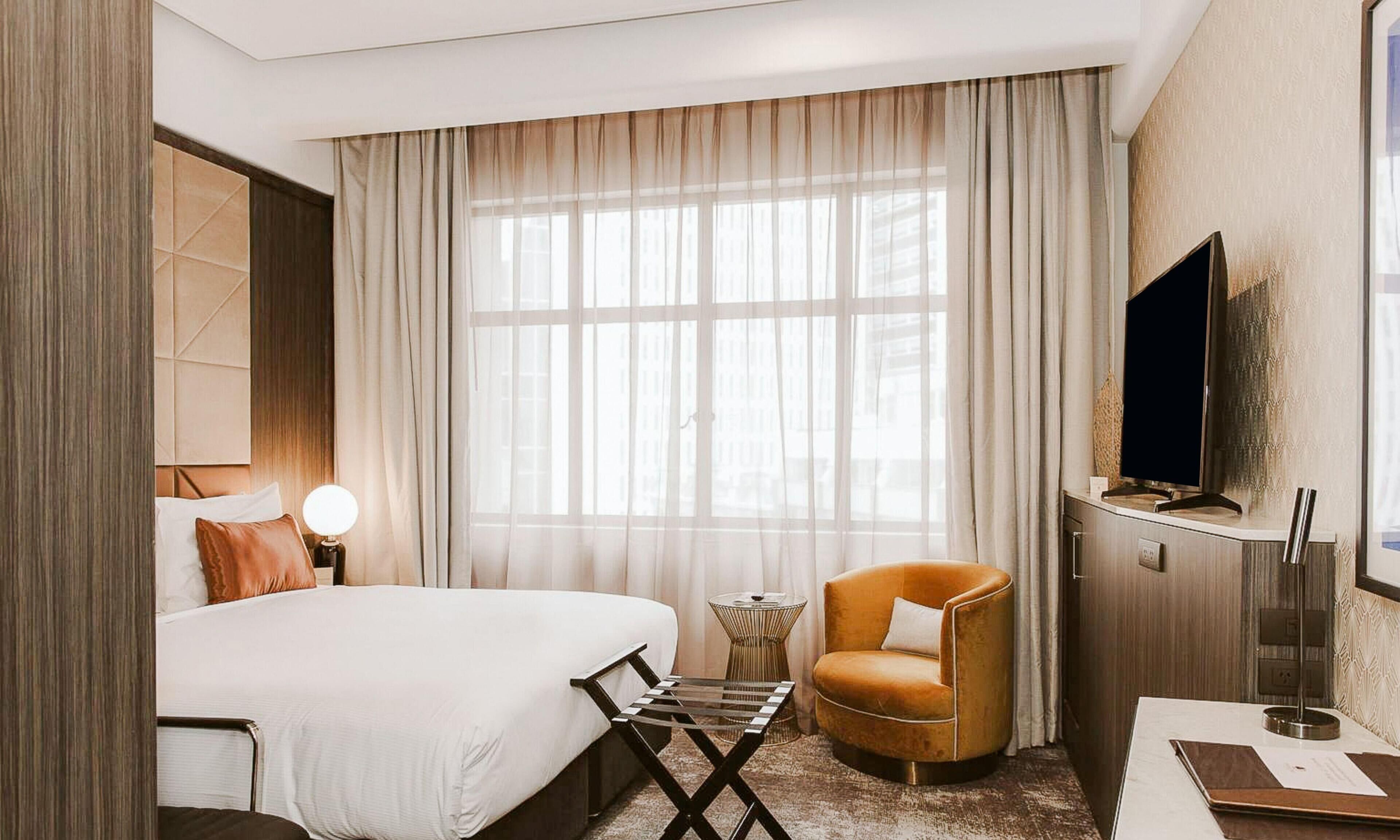 A hotel room with a bed, a TV, a chair, and a small table.