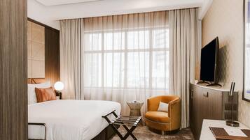 A hotel room with a bed, a TV, a chair, and a small table.