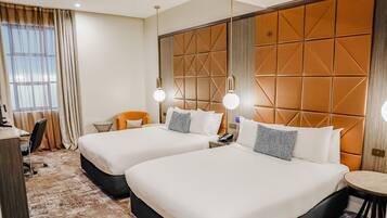 A hotel room with two beds, a desk, a chair, and a small table.